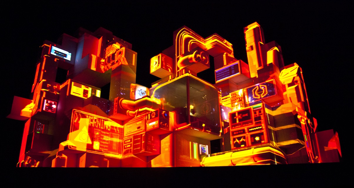 Amin Tobin incorporates the use of new video mapping techniques that are projected onto a large cubic structure from which he performs.